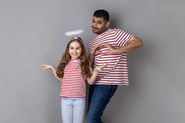 Portrait of optimistic father and daughter in striped T-shirts posing together, little girl with...