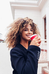 beautiful elegant afro business woman drinking coffee in the city smiling outdoors enjoying. curly-haired woman drinking coffee in the morning wearing elegant.