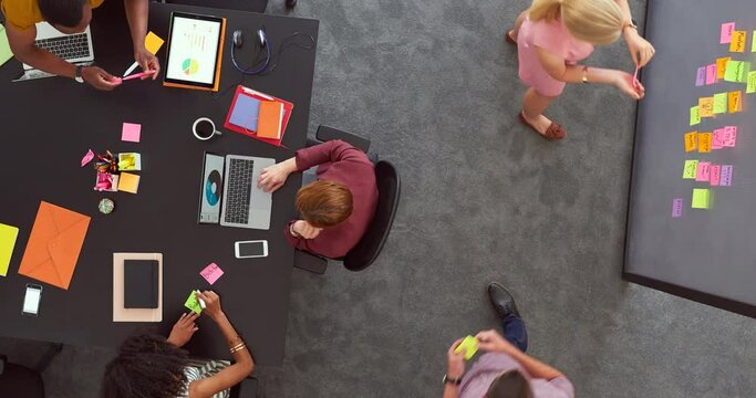 Time lapse of designers working in a trendy office from above. Overhead of a business man planning marketing ideas in busy creative agency and collaborating with diverse team of productive colleagues