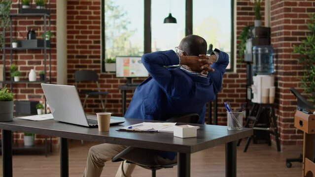 Businessman relaxing at office desk after working on project, sitting laid back on chair. Taking break from job feeling exhausted and overworked, timeout pause to relieve stress.