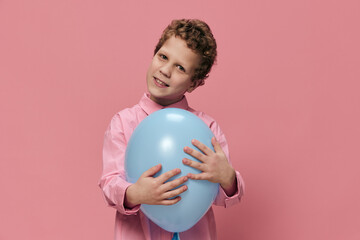 beautiful cute little boy of school age stands with a blue balloon in his hand and poses smiling...