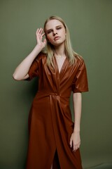 Fototapeta premium Sexy professional blonde model in leather brown palette clothes touching hair holding hand on head looks at camera posing isolated on over green studio background. Stylish portrait for banner design
