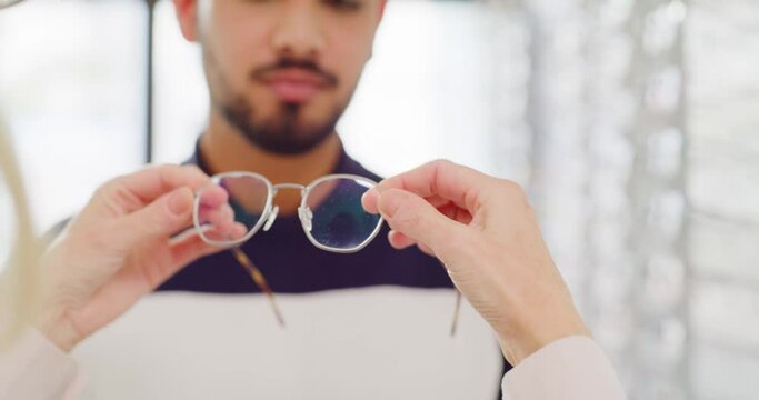 Optician fitting a pair of glasses on a man in an optical store. Optometrist choosing trendy spectacles from a shelf for customer. Trying on new prescription lenses for vision and eyesight correction