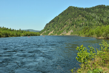 A wide river turns in a swift stream at the foot of a high mountain.