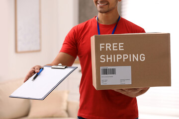 Young courier holding parcel and clipboard indoors, closeup. Free shipping
