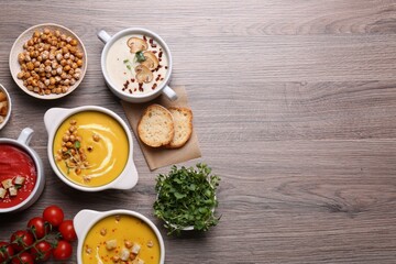 Different tasty cream soups and bread on wooden table, flat lay. Space for text