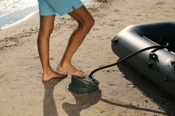 Man pumping inflatable rubber fishing boat at sandy beach on sunny day, closeup