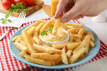 Woman dipping delicious French fries into cheese sauce at white table, closeup