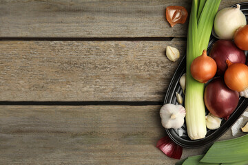 Plate with fresh onion bulbs, leeks and garlic on wooden table, flat lay. Space for text