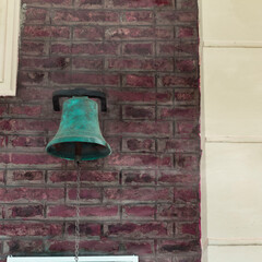 An old rusty bell hanging from a brick wall of an antique train station placed in a small rural town in Buenos Aires.