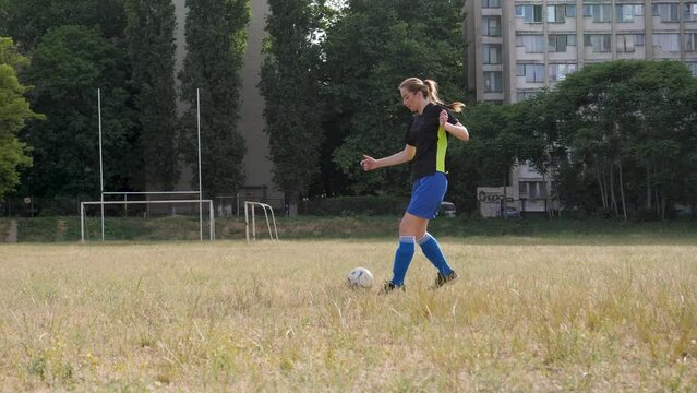 girl footballer dribbles the ball across an abandoned, not well-groomed football field
