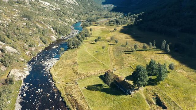 A tilt-shift video of a wide valley between tall mountains. A shallow river flows through the valley.