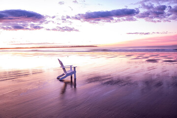 White wooden chair on the edge of the ocean at dawn. Gentle pink dawn. USA. Maine.
