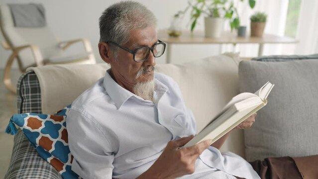 Asian senior older man with grey hair reading book at home morning
