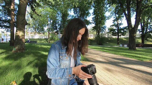 A beautiful young girl is sitting on a bench in the park looking at pictures on her camera