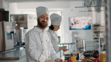 Authentic portrait of professional chef preparing celery for gourmet dish in restaurant kitchen, using organic ingredients. Smiling man cooking culinary recipe meal for gastronomy. Handheld shot.