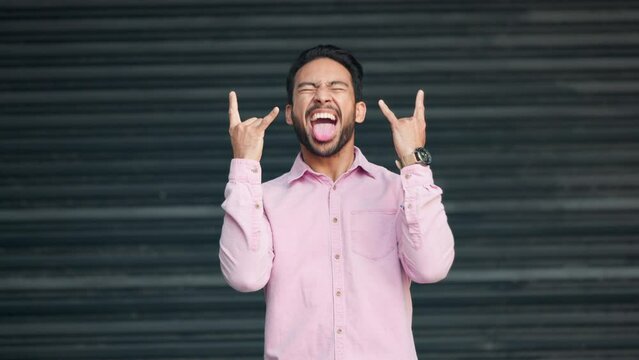 Excited punk fan listening to his favorite music, gesturing horns with his hands. Man shows love for rock and roll, sticks out tongue. Confident modern male enjoying his heavy metal song.