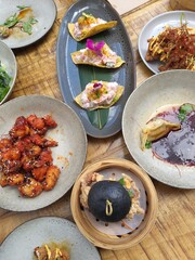 Asian fusion meal at a restaurant with dumplings chicken and bun on pretty ceramic plates