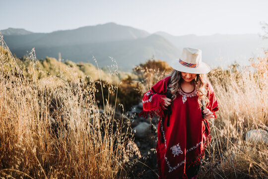 Latin backpacker woman wearing a traditional red poncho and a hat in a sunny landscape. Copy space