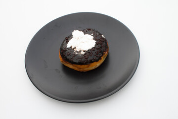 Chocolate donut cake filled with white cream on a black round plate on a white background