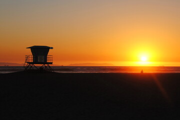 A lifeguard tower on a californian beach at sunset.  A man is sitting and watching sunset over the...