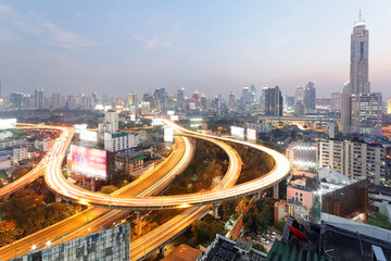Panorama of Bangkok at dusk with skyscrapers in background and traffic trails on elevated expressways and circular interchanges ~ Bangkok at rush hour with busy traffic on intertwined highway overpass