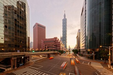 Fototapeta na wymiar Cityscape of Downtown Taipei, the capital city of Taiwan, with 101 Tower & World Trade Center standing in XinYi Financial District at sunrise and cars dashing thru the intersection in morning twilight