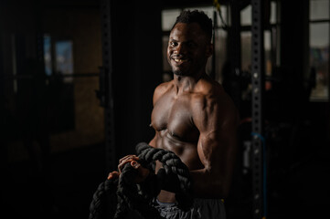 Muscular african american man posing with rope in gym. 