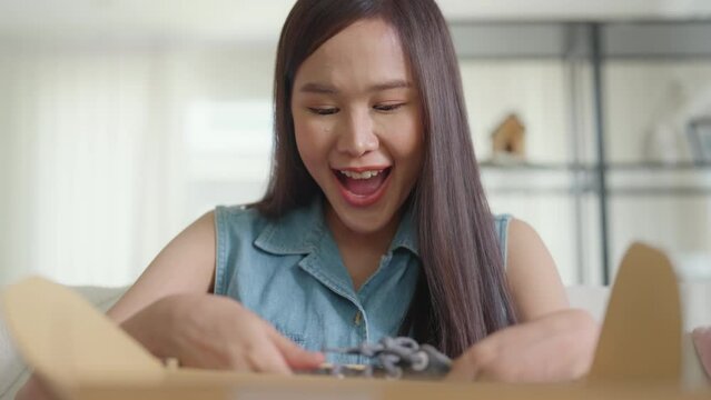 Young Gen Z influencer girl open gift postal mail box sit at home sofa couch. Asia people enjoy wow unbox carton parcel order online buy from small retail store SME shop supply chain omni channel.