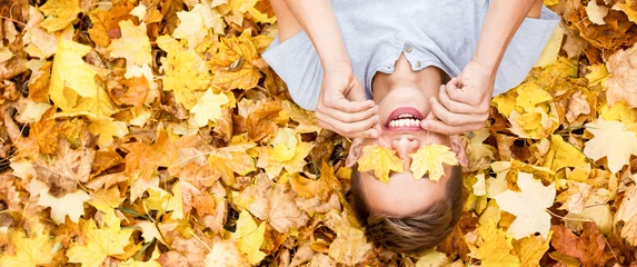 Poster Happy teenager in white t-shirt relax autumn season. lies and smiles at the autumn golden leaves in park. concept calm and peace. Caucasian guy in on fallen wedge leaves sunny day. photo banner © Евгений Гончаров