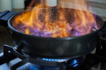 Beef meat fried with onions in frying pan, flambe on gas stove