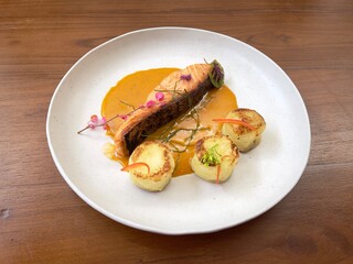 Salmon steak and red curry sauce, served with mashed potatoes and decorated with edible flowers and leaves. Fine dining main course. Selective focus