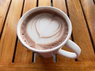 Hot chocolate, top view. Hot drink with heart shaped latte art in white mug on wooden table, top view.