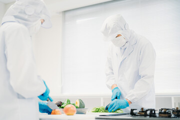 クリーンスーツで野菜のカットをする男女（食品加工）
