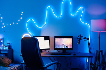 Horizontal image of place of streamer with computer monitors with video game and microphone in dark room decorated neon lights