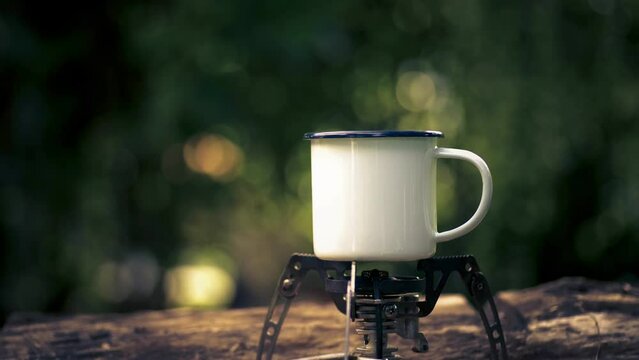Hot coffee in a white enamel mug on the gas stove in a camping atmosphere. soft focus.shallow focus effect.
