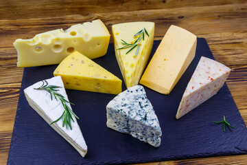Set of various types of cheese on black slate board on a wooden table