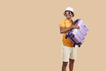Happy afro american male tourist or traveler holding suitcase on beige background. Joyful...