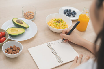 Diet, Dieting hand of asian young woman, girl write diet plan nutrition on table is different food ingredients in the green. Nutritionist of healthy, nutrition of weight loss, health care people.