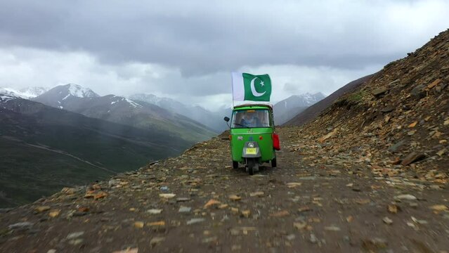 Drone shot of a Tuk Tuk on Babusar pass in Pakistan, with a few vehicles on the road below in the Kaghan Valley, on a dangerous rocky road, rising over Tuk Tuk revealing wide shot