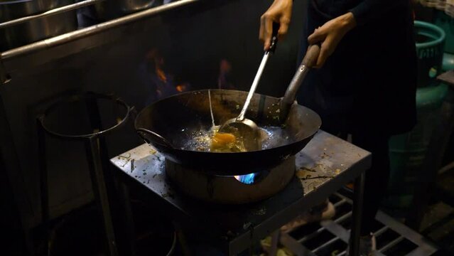 Chef stir frying eggs in wok on open fire, night market in Thailand, slow motion