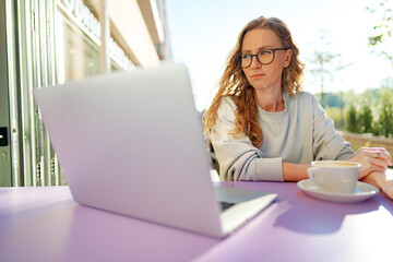 Smart woman in glasses sitting in cafe using laptop