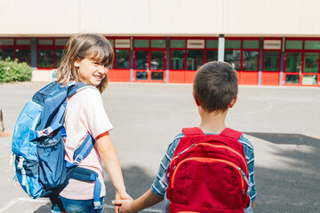 Close-up from the back of a brother and sister with backpacks on their backs going to school. The...