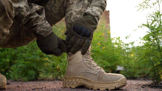 a soldier in a camouflage uniform and tactical gloves laces up his military boots. tactical footwear in combat conditions. preparation for a long-distance combat march. running in combat conditions