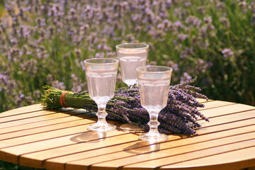 Three glasses of lavender cocktail are on the table, next to it lies a bouquet of lavender flowers. The table stands in a lavender field. Excellent atmosphere for relaxation, self-knowledge, rest, rec