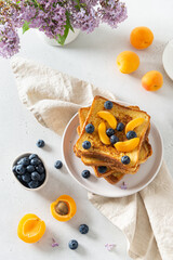 Tasty french toasts with blueberry, apricots and maple cyrup, a cup of coffee on the table with lilac bouquet. Trendy breakfast offer background. Bakery, reataurant menu. Top view