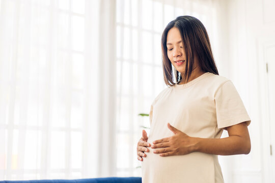 Asian mother woman hugging and smiling expecting with pregnancy hold baby in belly at home