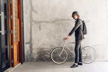 Portrait of hipster handsome businessman in suit with backpack walk and hold riding bicycle on the...