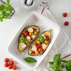 Grilled eggplants with mozzarella, tomatoes, basil and olives in baking dish on white background. Aubergine seasonal vegan recipe. Dieting, healthy nutrition. Restaurant menu. top view, square