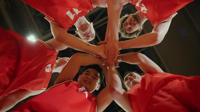 Slow motion, red team of basketball players shouts chants and raising morale before the game, the international basketball championship, view from the lower angle.